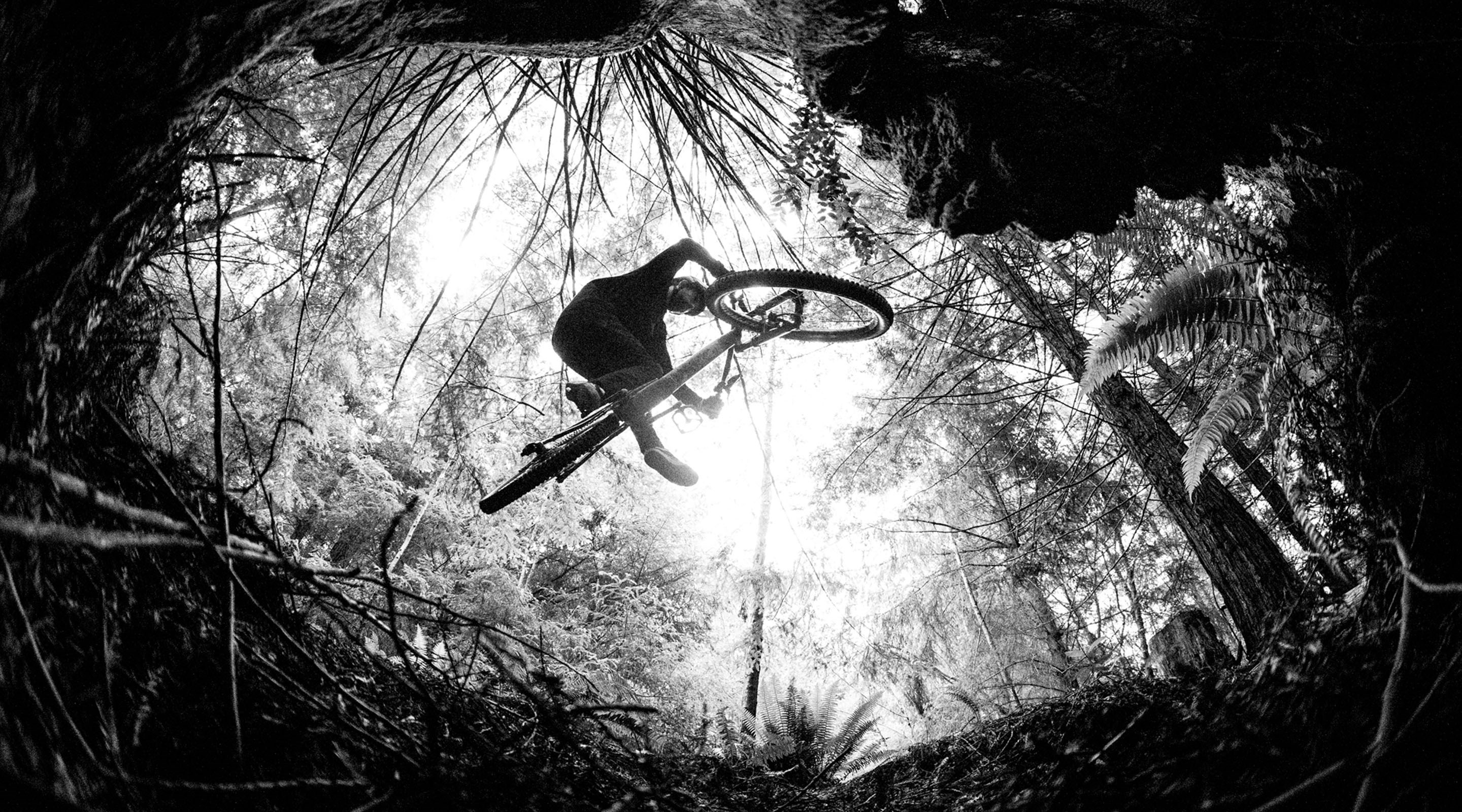 Black and white image of a MTB rider in mid air from below.