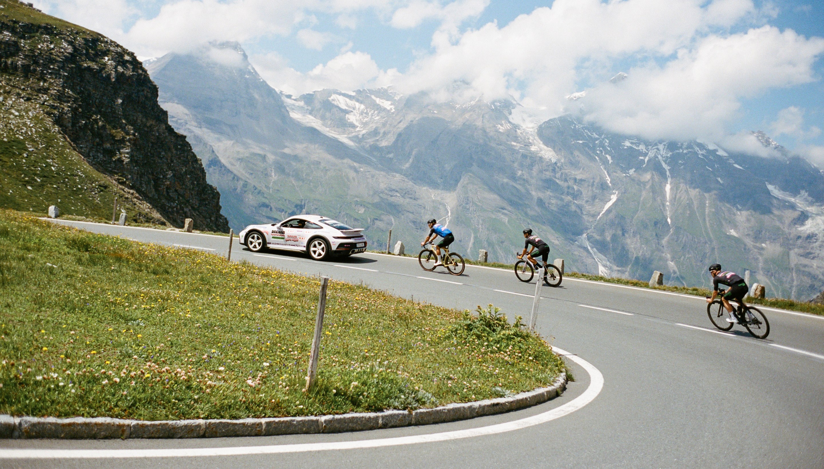 3 riders trailing a Porsche up Giro di Mankei hill climb