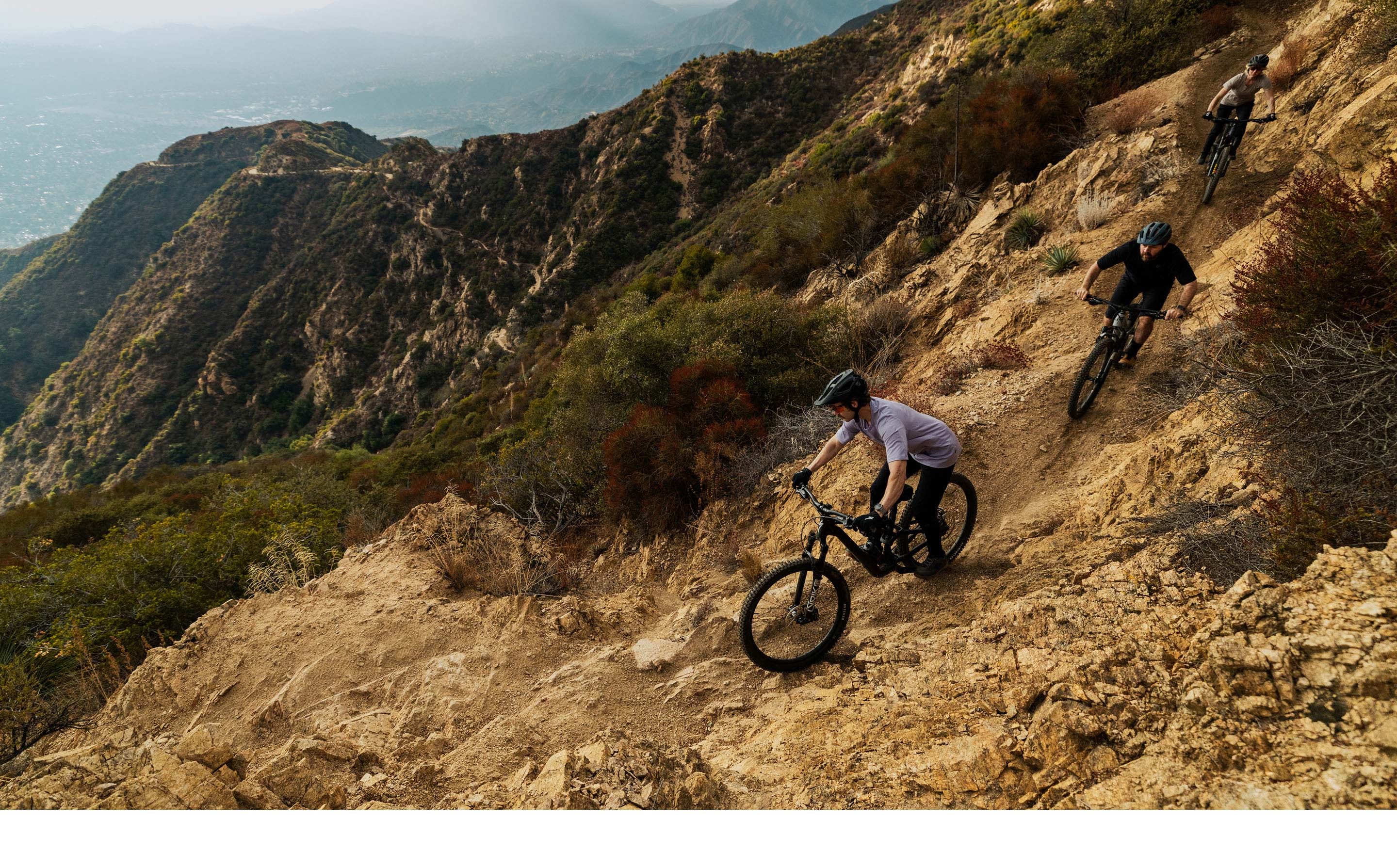 Three riders descending a MTB trail on rocky landscape.
