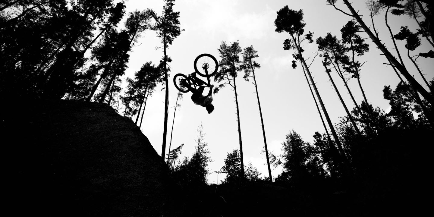 A black and white photo of Kade Edwards backflipping a jump.