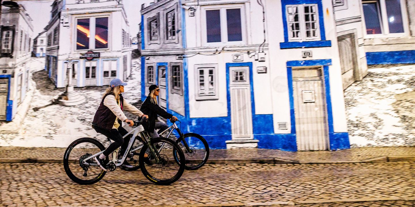 Side shot of Vali Höll and Cécile Ravanel riding against a painted building in Portugal.