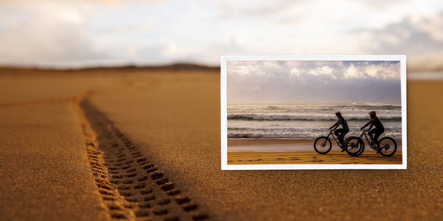 (Picture) Vali Höll and Cécile Ravanel riding on a beach. (Background image) Bike tracks in the sand on the beach.