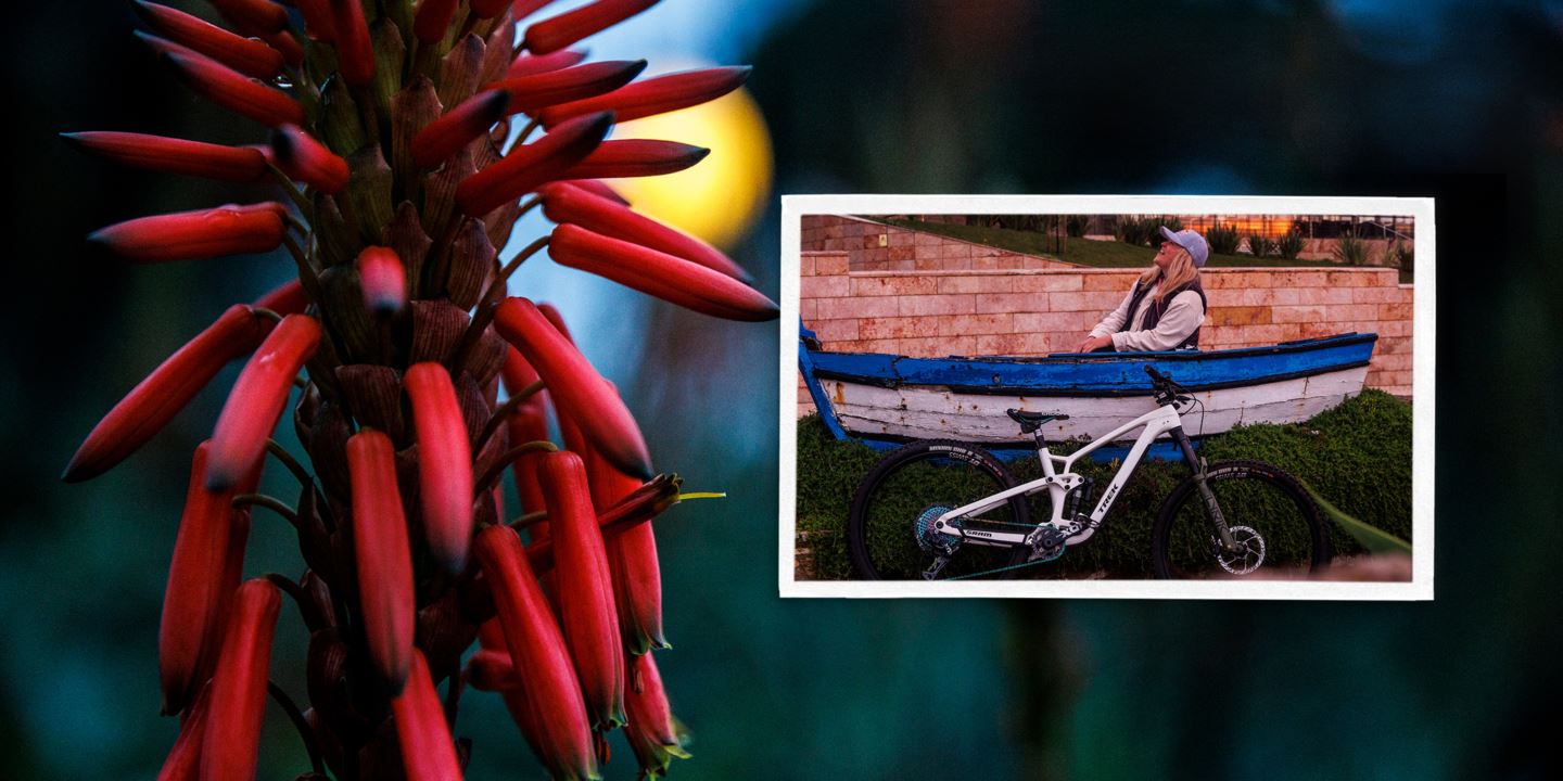 (Picture) of Vali Höll sitting in a canoe with her Trek Fuel EX leaning against it. (Background) a red  plant.
