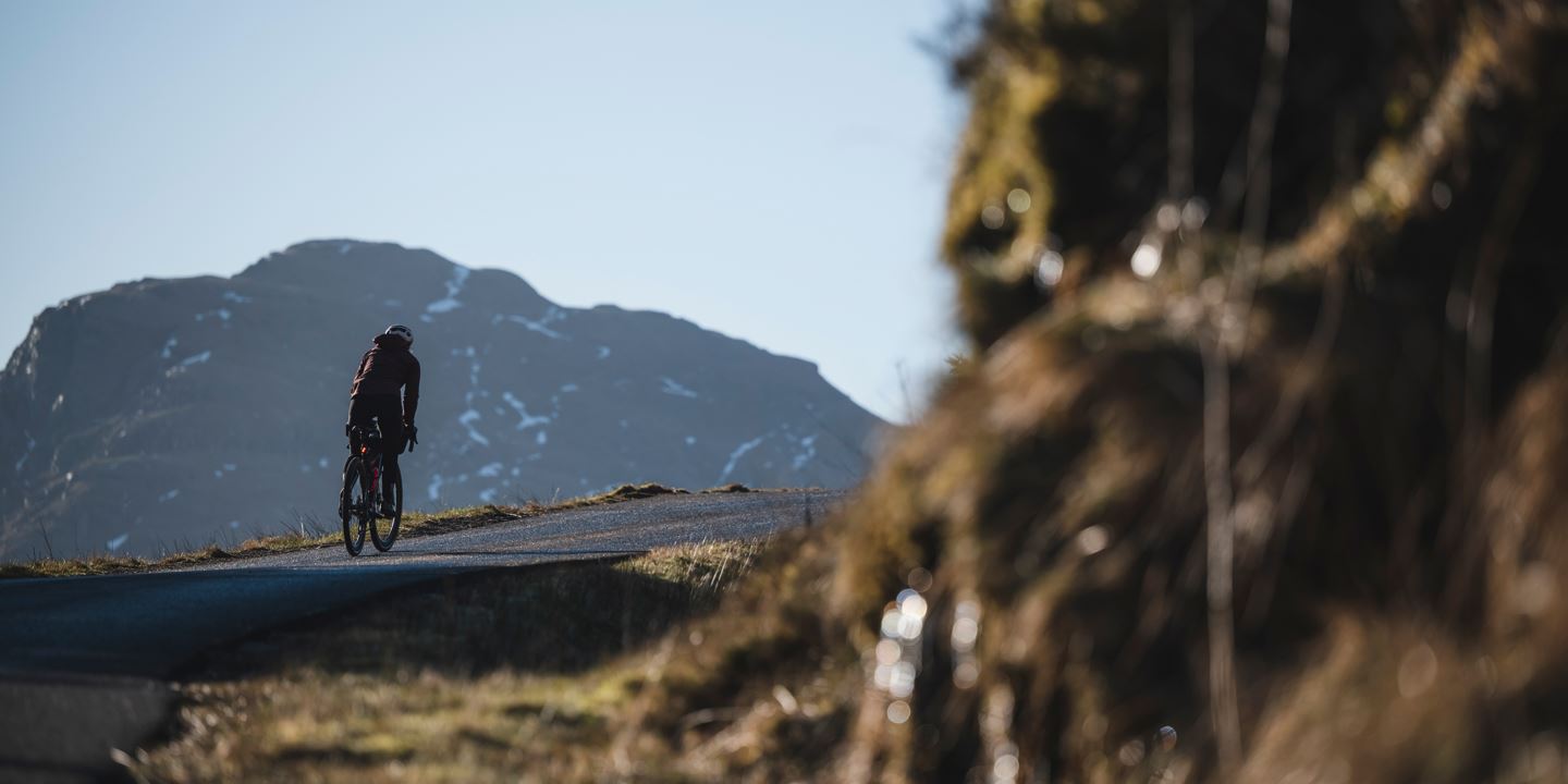 Rachael Walker riding uphill on tarmac into the shade of the mountain.