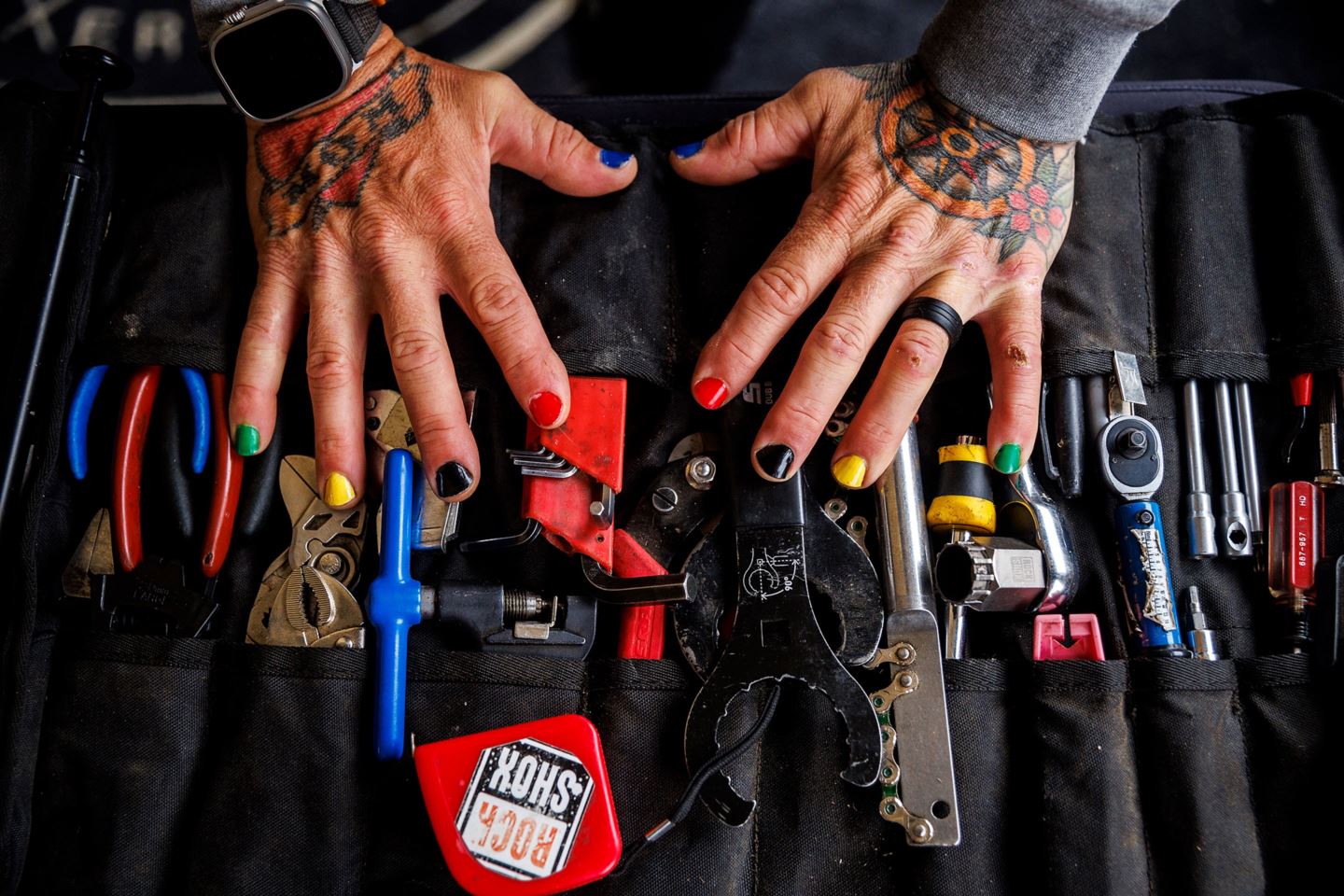 JT Evans' (Tegan's mechanic) hands with nails painted like the rainbow stripes over his set of tools.